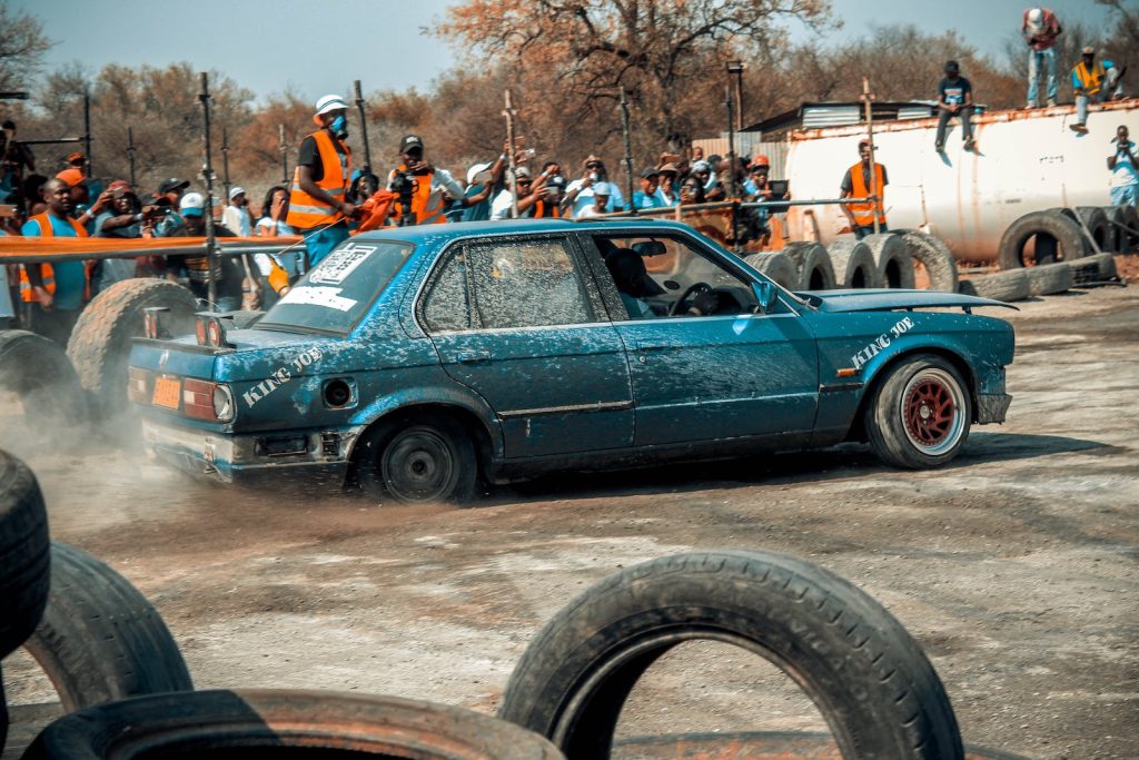 Blue Sedan Doing Burnout on Sand Near People
