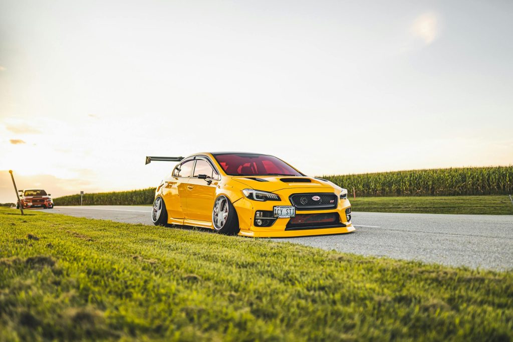 Customised yellow sports car parked on a rural road with green fields under a clear sky