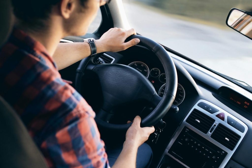 Person driving a car, holding the steering wheel, interior dashboard visible